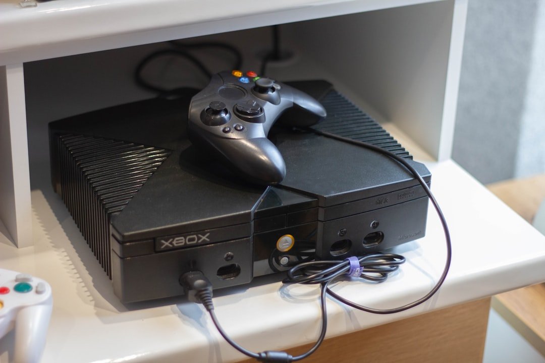 Black video game console with a controller on a white shelf